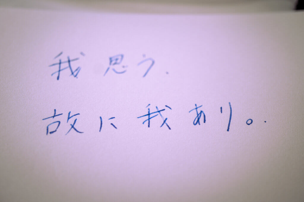 『我思う。故に我あり。』と青インクで書かれた文字のアップ写真（浅いピント）
